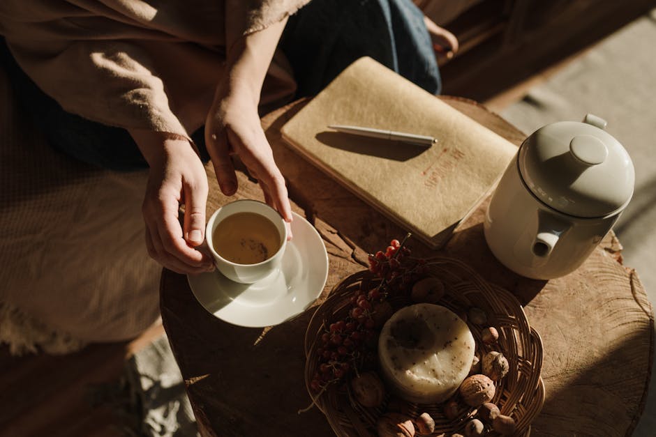 Cozy indoor setting with hands holding tea, notebook, and teapot, basking in warm autumn sunlight.