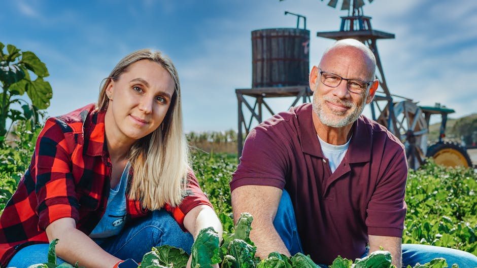 Two farmers smiling while tending crops in a rural countryside farm.