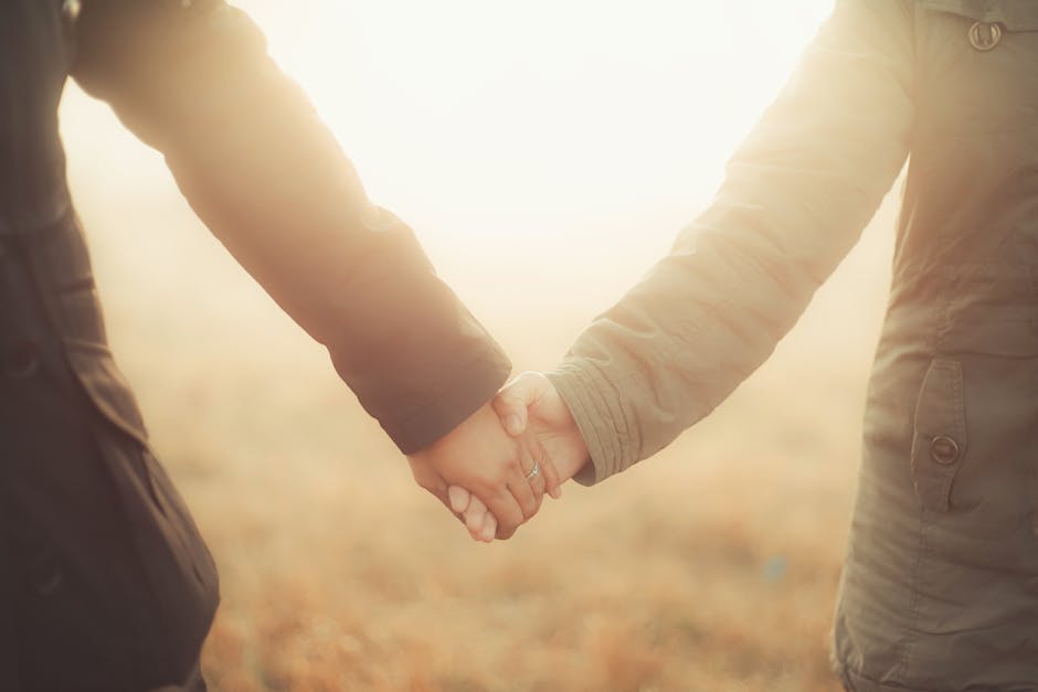 A warm and intimate close-up of a couple holding hands outdoors during sunset.