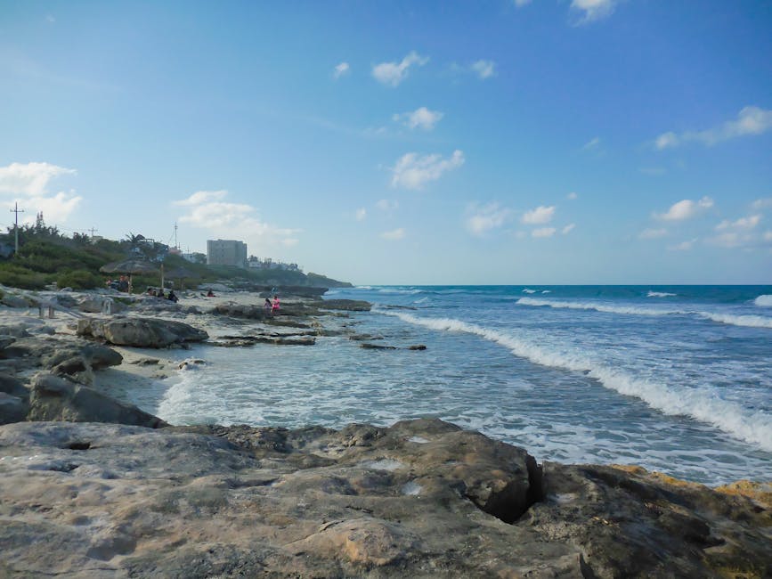 A peaceful beach scene with rocky shoreline and gentle waves under a bright blue sky.