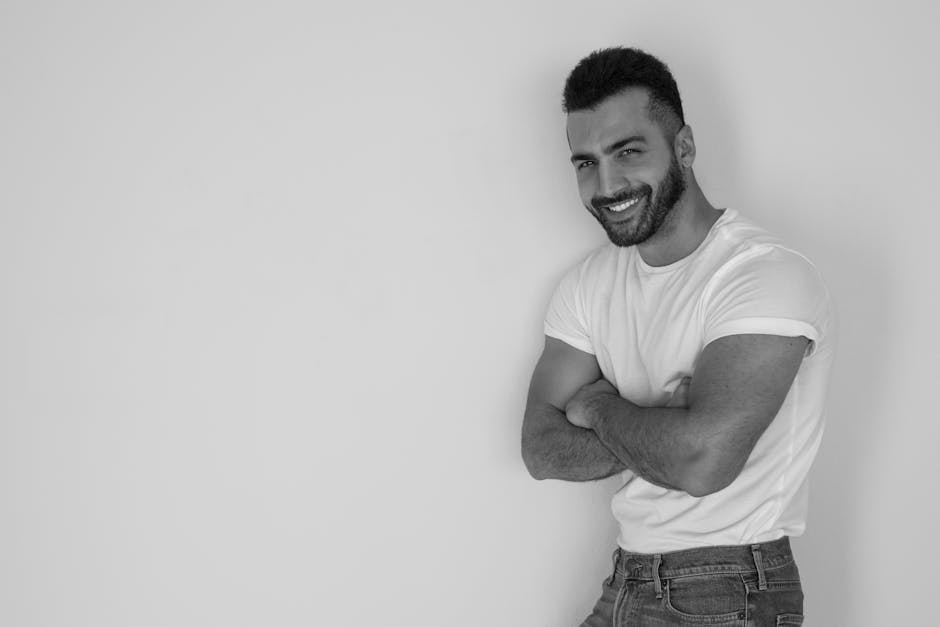 Monochrome portrait of a stylish man with arms crossed, exuding confidence in a studio setting.