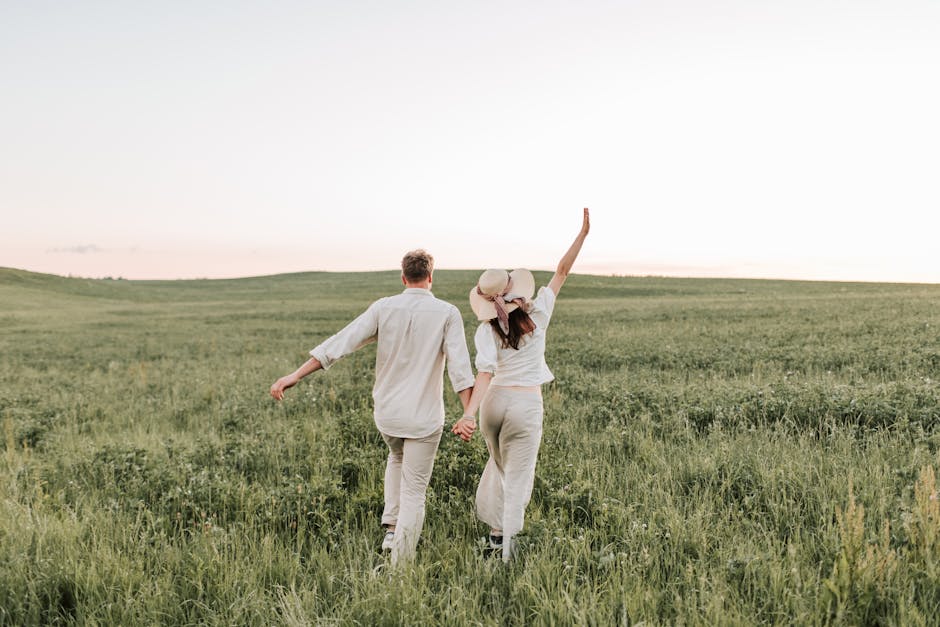 A couple enjoying a romantic walk in a sunlit field, holding hands in nature.