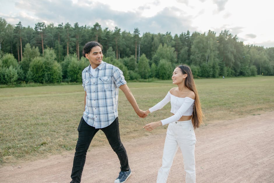 Joyful couple walking hand in hand through a lush park setting, under a bright sky.