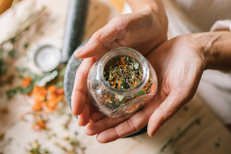 Close-up of hands holding a glass jar filled with colorful dried herbs.