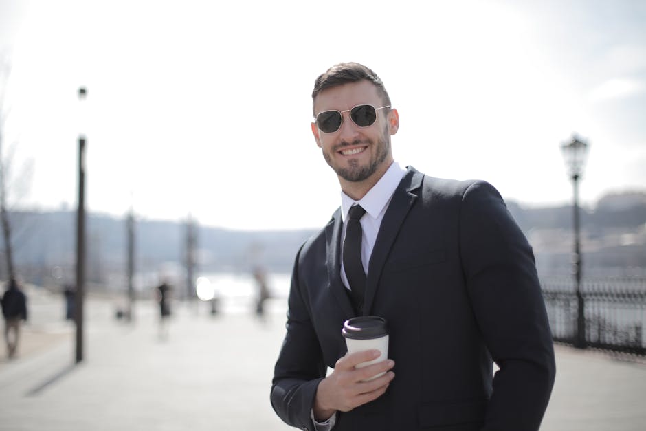 Businessman in a suit and sunglasses smiling while holding coffee cup outdoors.