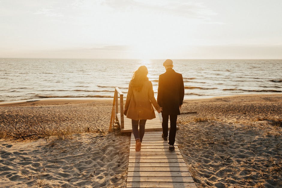 A couple walks hand in hand along a sandy beach during a beautiful sunset, symbolizing togetherness.