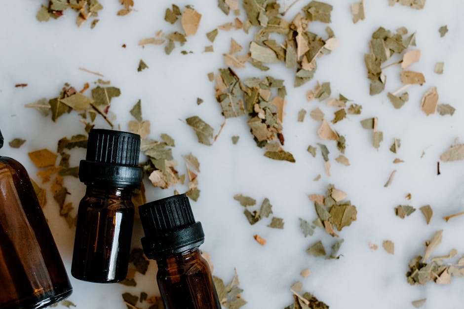 A flat lay of essential oil bottles with scattered dried herbal leaves on a white background.