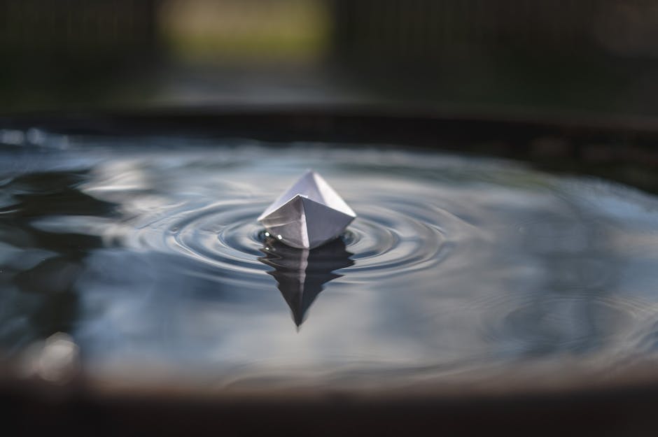 Peaceful image of a paper boat floating on calm water with gentle ripples around it.