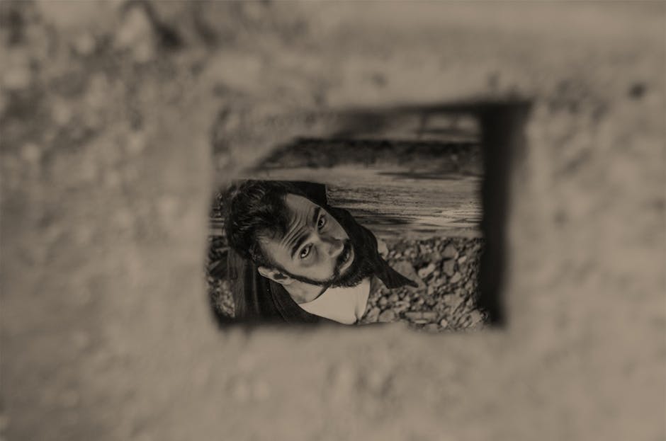 Sepia-toned portrait of a man looking up through a hole, creating a dramatic artistic effect.