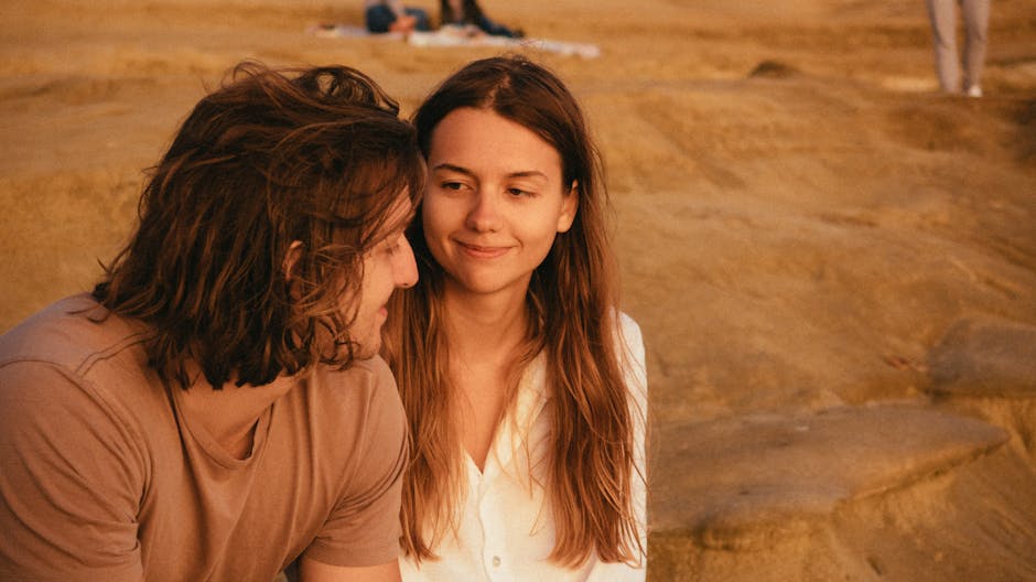 A young couple sharing a moment of connection during sunset on a sandy landscape.