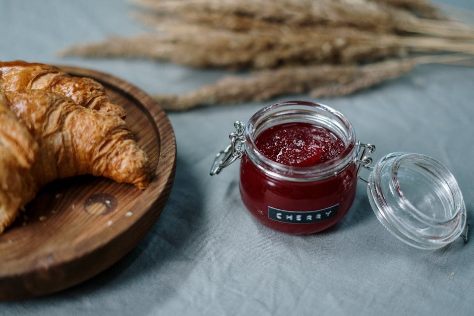 Delicious croissants on wooden plate with cherry jam jar on rustic table.