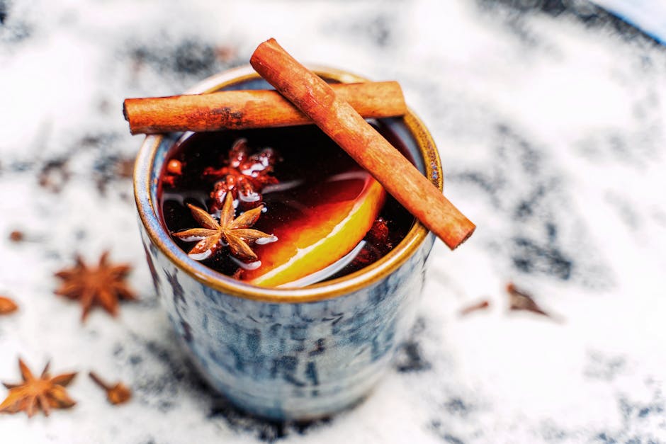 Close-up of a warm spiced beverage garnished with cinnamon sticks and star anise in a rustic cup.