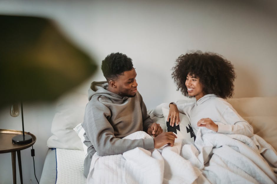 Cheerful couple enjoying a cozy morning in bed, wrapped in soft blankets, sharing smiles and warmth.