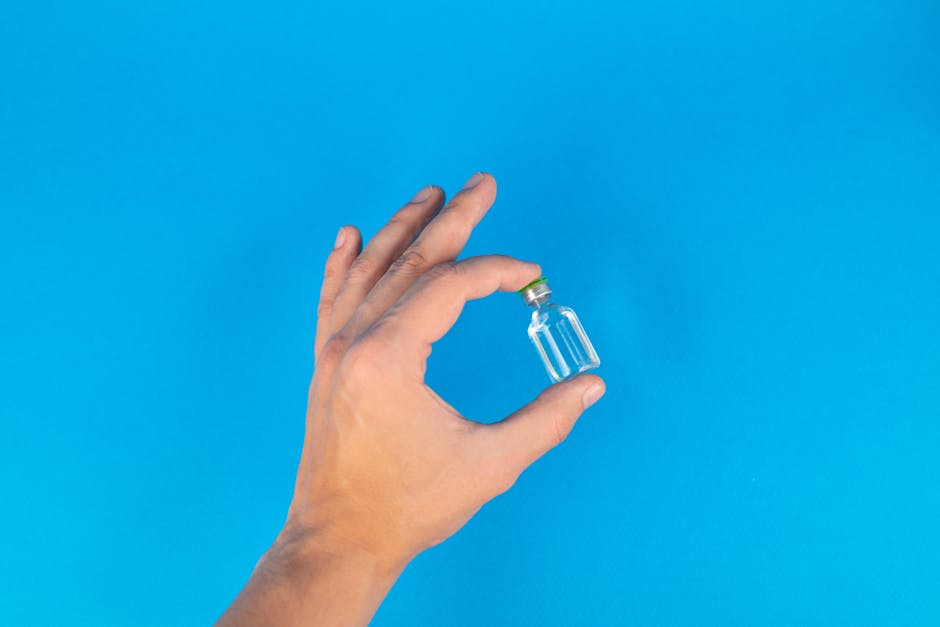 Close-up of a hand holding a tiny glass bottle against a bright blue background.