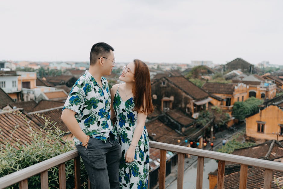 Asian couple dressed in matching outfits enjoying a rooftop view of a picturesque town.