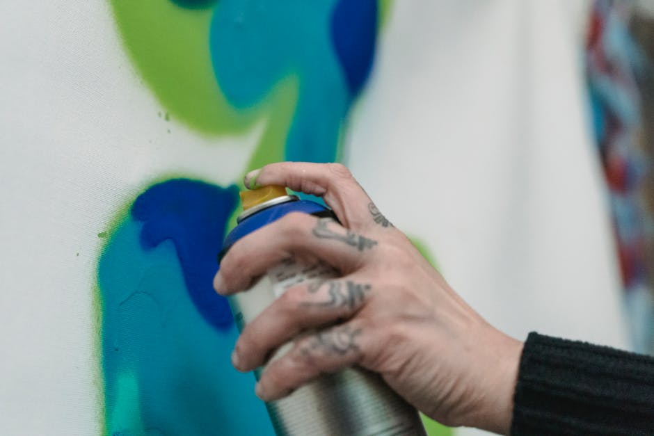 A detailed close-up of a hand spray painting vibrant colors on canvas.