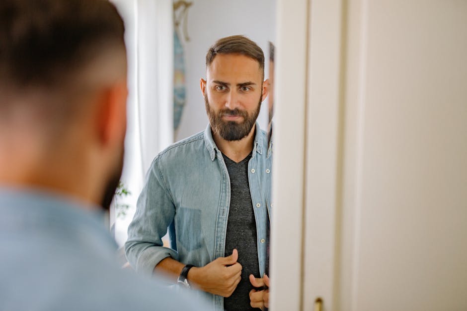 Man with a beard adjusting his shirt in front of a mirror at home, reflected image.
