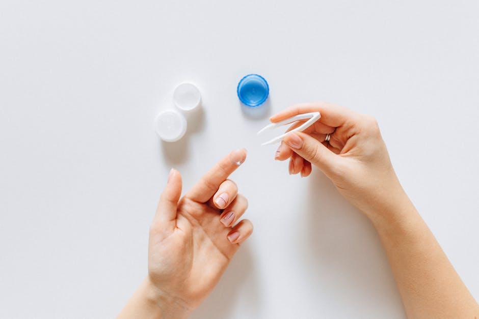 Close-up of hand using tweezers with contact lens and lens case on a white background.