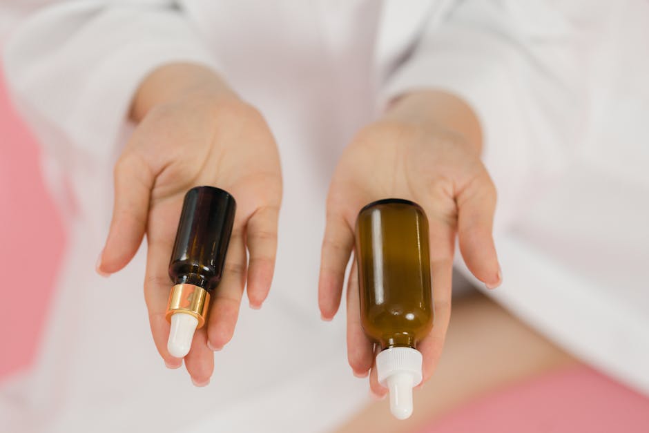 A close-up of hands holding two glass skincare bottles on a soft pink background.