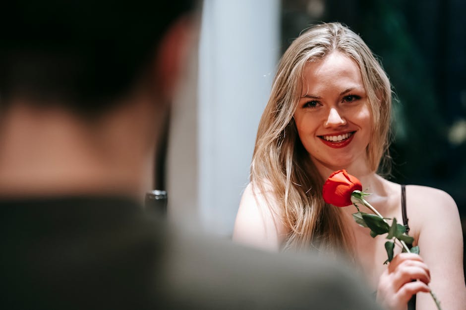 Smiling woman with a red rose in a romantic indoor setting, perfect for Valentine's celebration.