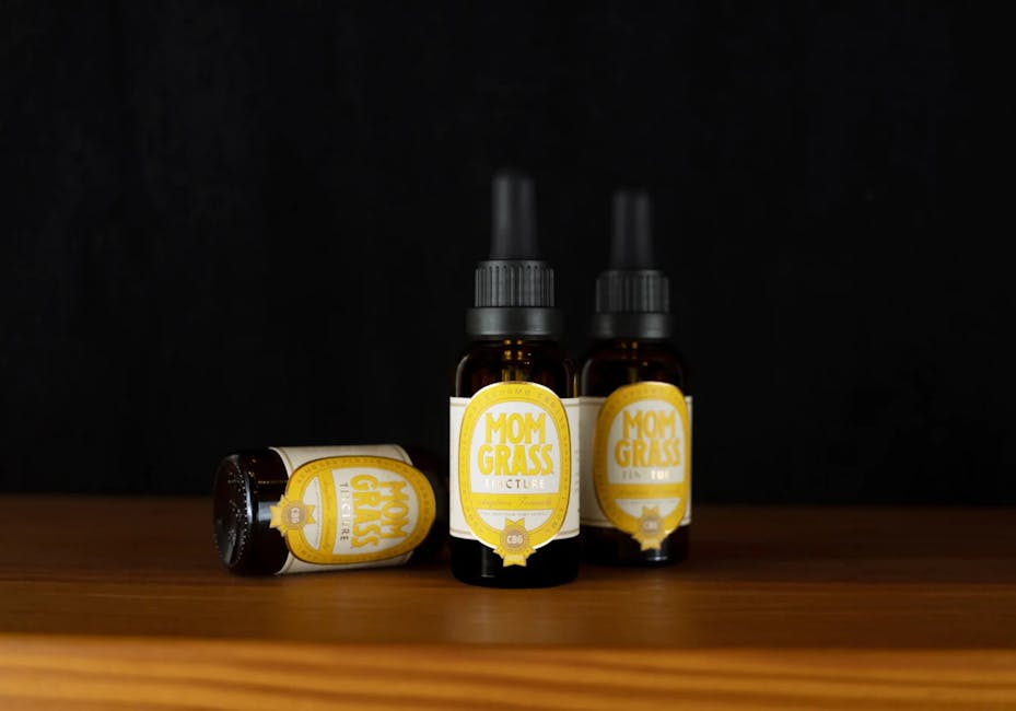 Close-up of CBD dropper bottles labeled 'Mom Grass' on a wooden surface.