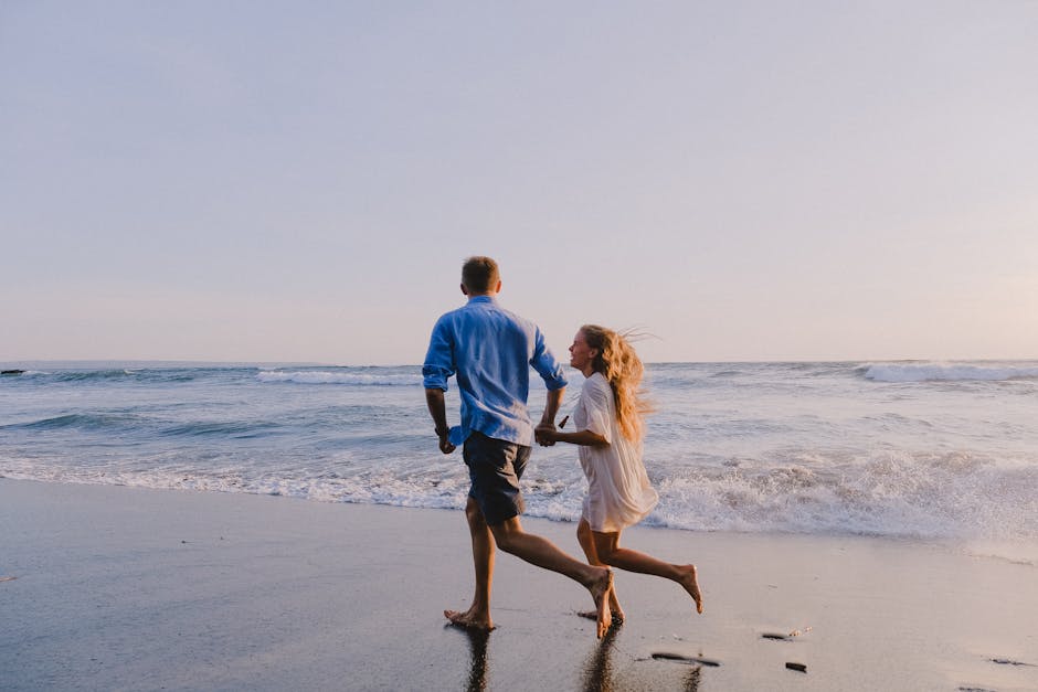 A couple runs barefoot along the beach, enjoying a romantic sunset by the ocean.